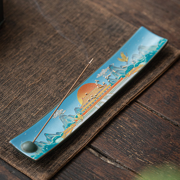 Palace-pattern enamel incense tray with a burning stick on a wooden table
